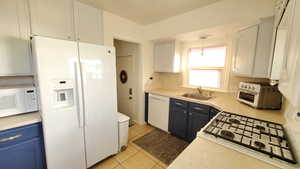 Kitchen featuring white appliances, light countertops, pendant lighting, light tile patterned floors, and white cabinets