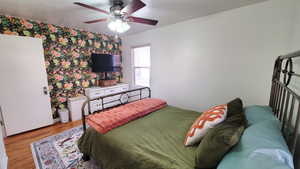 Bedroom with wallpapered wall, wood finished floors, and a ceiling fan