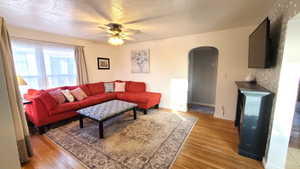 Living room with arched walkways, a textured ceiling, light wood finished floors, and ceiling fan