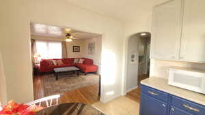 Kitchen with white microwave, arched walkways, light countertops, a ceiling fan, and light tile floors