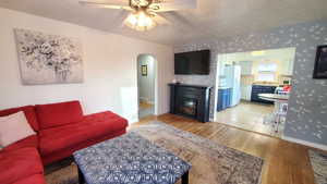 Living room with light wood-style floors, hand painted walls, arched walkways, a glass covered fireplace, and a textured ceiling