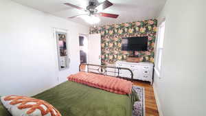 Bedroom with wood finished floors, wallpapered walls, an accent wall, and ceiling fan