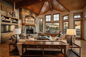 Living room with hardwood / wood-style flooring, a stone fireplace, high vaulted ceiling, and a wood ceiling with exposed beams
