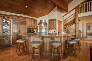 Kitchen with a kitchen breakfast bar, dark stone countertops, paneled refrigerator, a vaulted wooden ceiling, and light wood-style floors