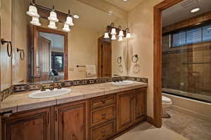 Bathroom with double vanity, connected bathroom, shower / bath combination with glass door, a textured wall, and recessed lighting