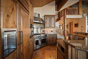 Kitchen featuring appliances with stainless steel finishes, dark stone counters, wall chimney exhaust hood, vaulted ceiling, and dark wood-type flooring