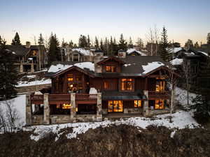 Snow covered property with stone siding, view of wooded area, a balcony, and a residential view