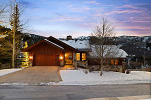 View of front of home with stone siding, board and batten siding, concrete driveway, a garage, and a chimney