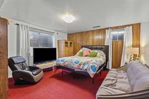 Carpeted bedroom with wood walls, multiple windows, and a textured ceiling
