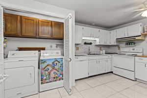 Kitchen with white appliances, decorative backsplash, under cabinet range hood, a ceiling fan, and light tile patterned floors