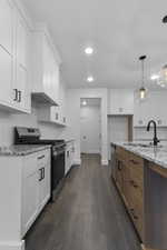 Kitchen featuring stainless steel appliances, light stone counters, white cabinets, dark wood-type flooring, and decorative light fixtures