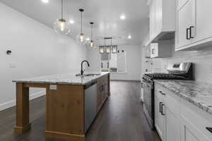 Kitchen with stainless steel appliances, white cabinets, light stone counters, pendant lighting, and an island with sink