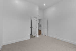 Unfurnished bedroom featuring light colored carpet, a towering ceiling, and recessed lighting