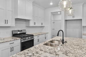 Kitchen featuring stainless steel gas stove, decorative backsplash, white cabinetry, light stone counters, and recessed lighting