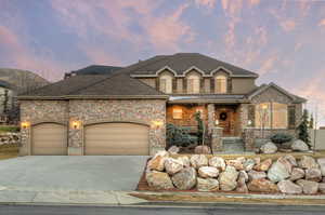View of front of house with covered porch, concrete driveway, stone siding, a shingled roof, and a garage