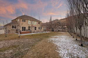 Back of property at dusk with a patio area, a lawn, stucco siding, and stone siding
