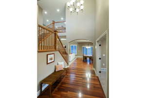 Foyer with a chandelier, stairs, dark wood-style floors, arched walkways, and a high ceiling