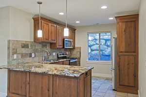 Kitchen with dark stone countertops, brown cabinetry, appliances with stainless steel finishes, a peninsula, and decorative light fixtures