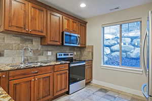 Kitchen featuring stainless steel appliances, light stone countertops, tasteful backsplash, brown cabinetry, and recessed lighting