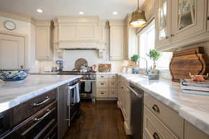 Kitchen featuring cream cabinets, high end appliances, hanging light fixtures, dark wood-style floors, and glass insert cabinets