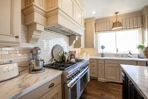 Kitchen featuring range with two ovens, cream cabinets, dark wood finished floors, pendant lighting, and light stone countertops