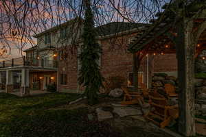 Back of property at dusk with a patio area, brick siding, a lawn, and a balcony