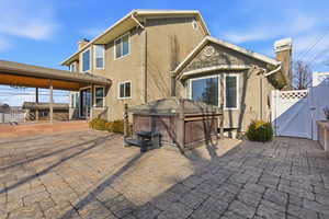 Back of house featuring a  salt water hot tub with electric cover, a chimney, a gate, stucco siding, and a patio