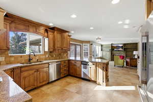 Kitchen featuring brown cabinets, light stone countertops, appliances with stainless steel finishes, a peninsula, and recessed lighting