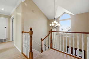 Hall featuring an upstairs landing, carpet floors, a chandelier,  lofted ceiling, and natural light