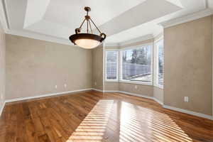 Large dining  room featuring light wood-style flooring, ornamental molding, tray ceiling,  and natural lighting