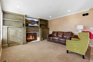 Carpeted living area featuring custom built in shelves, a gas fireplace, recessed lighting, and crown molding
