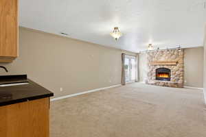 Unfurnished living room with a gas fireplace, crown molding, light colored carpet, a textured ceiling,, track lighting, and walk out basement.