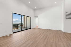 Empty room with light wood-style floors, a towering ceiling, recessed lighting, and a mountain view