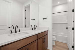 Full bath with double vanity, light wood finished floors,  shower combination, and recessed lighting