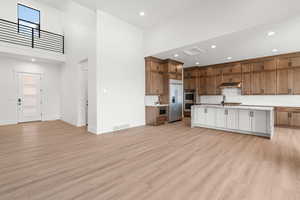 Kitchen with open floor plan, brown cabinetry, a high ceiling, a kitchen island with sink, and recessed lighting