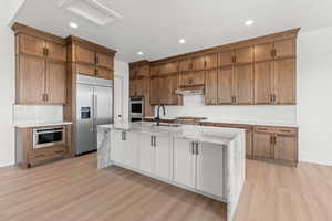 Kitchen featuring light stone counters, an island with sink, stainless steel appliances, backsplash, and recessed lighting