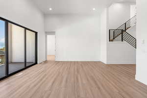 Unfurnished living room with a high ceiling, light wood finished floors, stairway, and recessed lighting