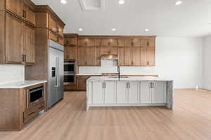 Kitchen featuring light stone countertops, tasteful backsplash, appliances with stainless steel finishes, a kitchen island with sink, and recessed lighting