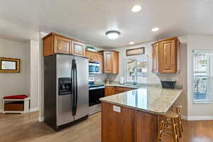 Kitchen featuring stainless steel appliances, light stone countertops, light wood-style floors, a breakfast bar area, and brown cabinets