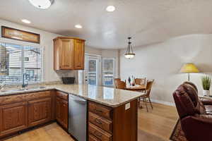 Kitchen with light stone counters, light wood-style floors, pendant lighting, stainless steel dishwasher, and open floor plan