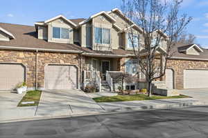 View of front facade featuring stone siding, a garage, concrete driveway, and covered porch