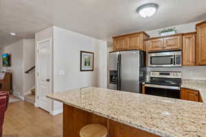 Kitchen featuring stainless steel appliances, brown cabinets, light stone countertops, light wood finished floors, and a textured ceiling