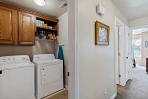 Laundry room with cabinet space, light colored carpet, and separate washer and dryer