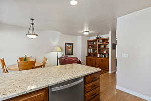 Kitchen with dishwasher, decorative light fixtures, light stone countertops, brown cabinetry, and a textured ceiling