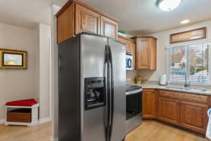 Kitchen with appliances with stainless steel finishes, brown cabinets, light wood finished floors, light stone counters, and a textured ceiling