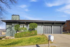 Mid-century inspired home featuring a chimney, concrete driveway, a front yard, and a garage
