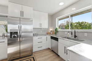 Kitchen featuring stainless steel appliances, light stone counters, light wood-style flooring, white cabinetry, and recessed lighting