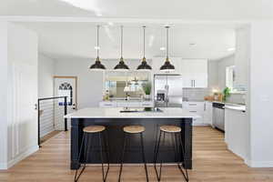 Kitchen featuring hanging light fixtures, white cabinets, a breakfast bar, backsplash, and a kitchen island