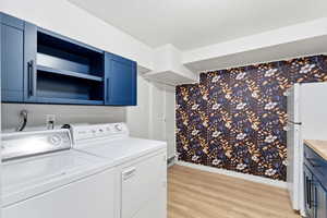 Laundry room with light wood-type flooring, washer and dryer, and wallpapered walls