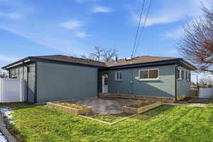 Rear view of house featuring a patio area, a vegetable garden, roof with shingles, and brick siding